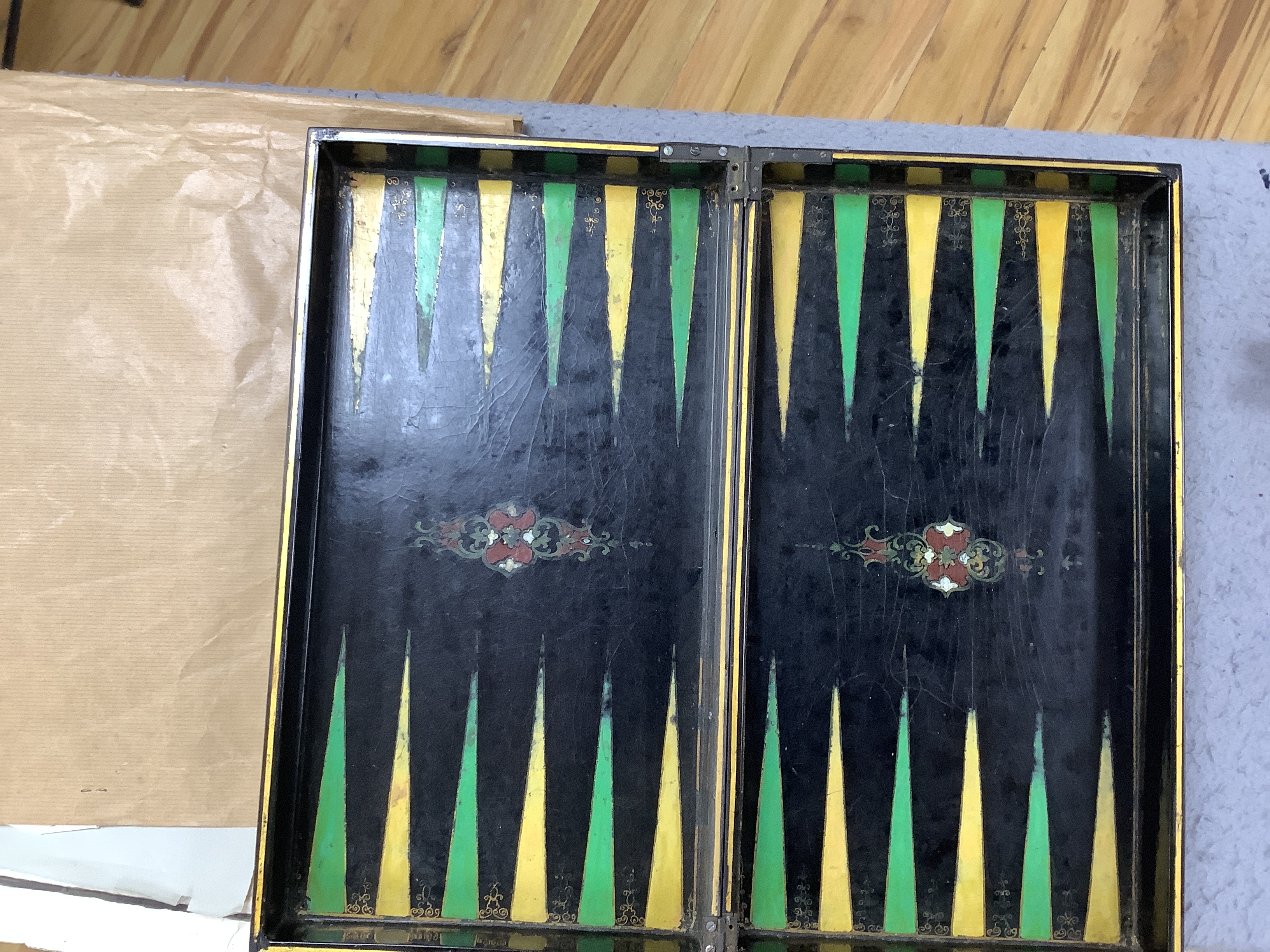 A 19th century papier maché folding games board for chess and backgammon, containing a wooden draughts set etc. with gilt decoration, 41 x 45cm unfolded